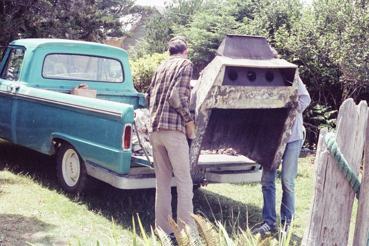 Image 6: Steve and Dave load the old "Heatalator" into Dave's pickup truck. The Heatalator has rusted out completely, and instead of sending warmed air into the cabin, it sent smoke and soot.