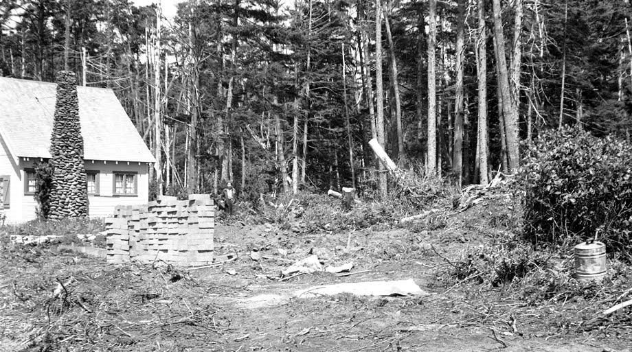 Concrete blocks for the Sullishak foundation have been delivered, and the Sullishak site has been cleared by a bull dozer leaving large piles of brush to the side and rear. Vera Lantz is just barely visible looking back at the camera from her home site’s location.